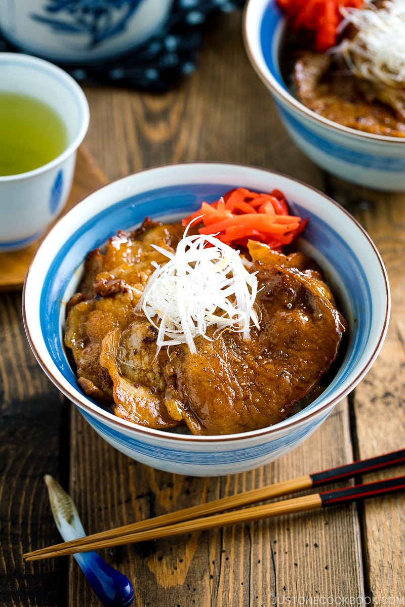 A Japanese bowl containing steamed rice, topped with soy-caramelized pork slices and pickled red ginger.