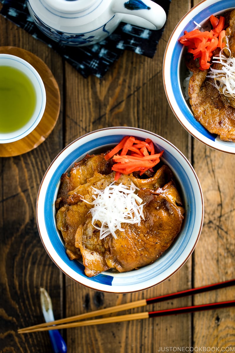 A Japanese bowl containing steamed rice, topped with soy-caramelized pork slices and pickled red ginger.