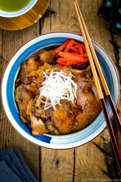 A Japanese bowl containing steamed rice, topped with soy-caramelized pork slices and pickled red ginger.