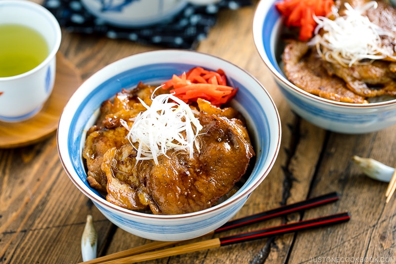 A Japanese bowl containing steamed rice, topped with soy-caramelized pork slices and pickled red ginger.