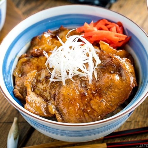 A Japanese bowl containing steamed rice, topped with soy-caramelized pork slices and pickled red ginger.