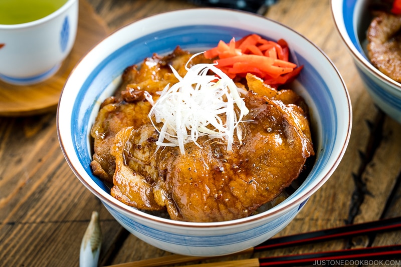 A Japanese bowl containing steamed rice, topped with soy-caramelized pork slices and pickled red ginger.