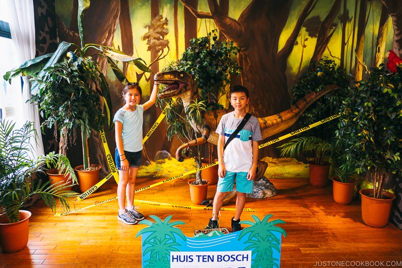 girl and boy in front of dinosaur sculpture and plants