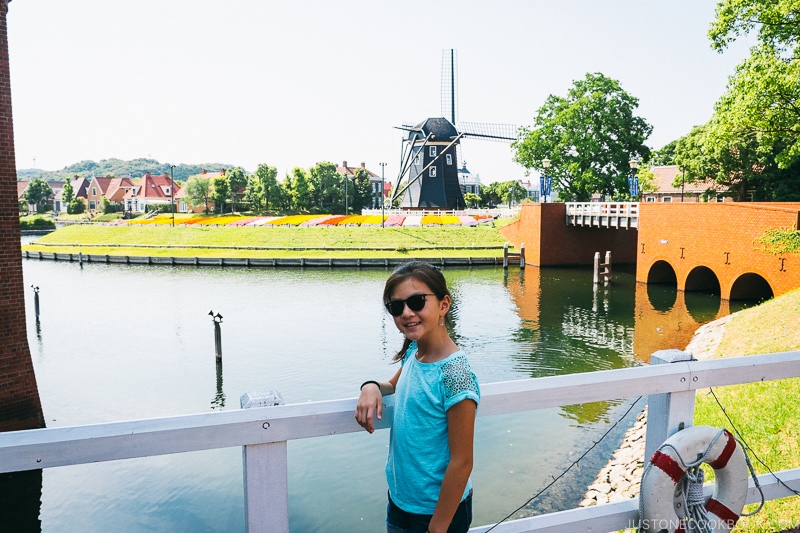 girl on a bridge in front of a body of water and windmill in the background