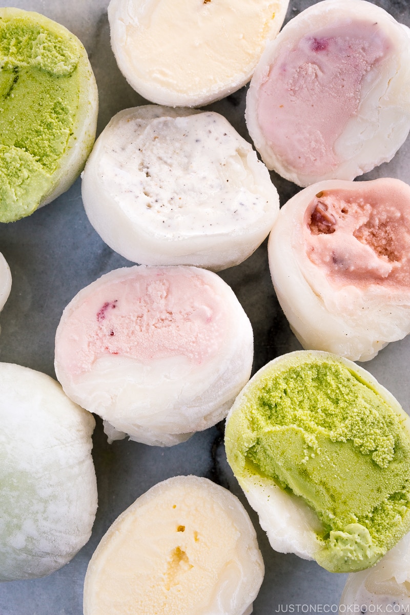 Variouso mochi ice cream cut in half and placed on the marble cutting board.