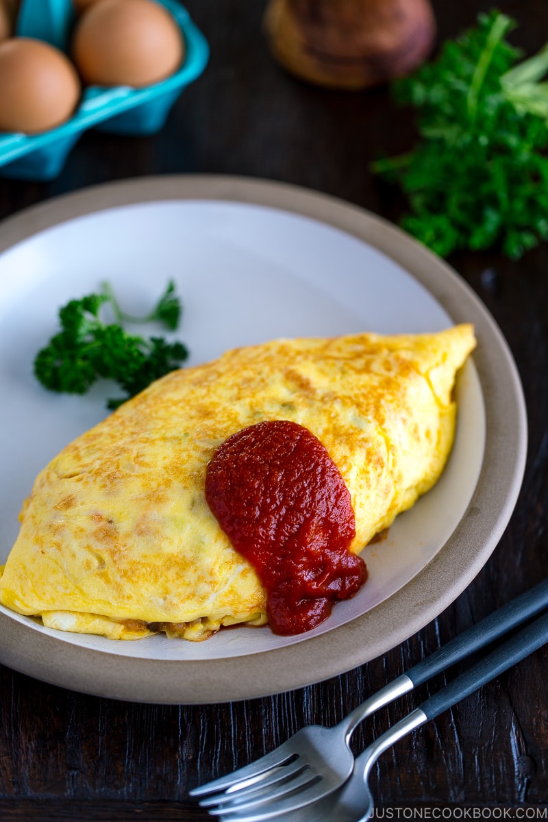 A plate containing Omurice, topped with tomato sauce and garnished with parsley.