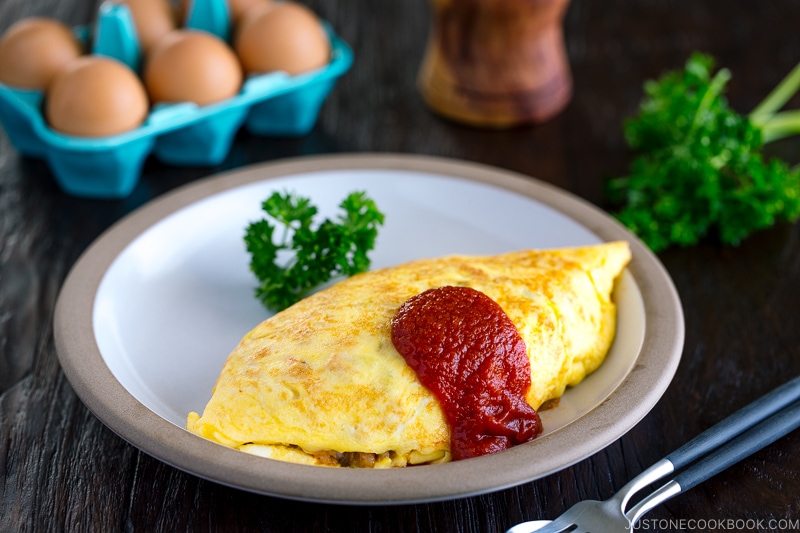 A plate containing Omurice, topped with tomato sauce and garnished with parsley.