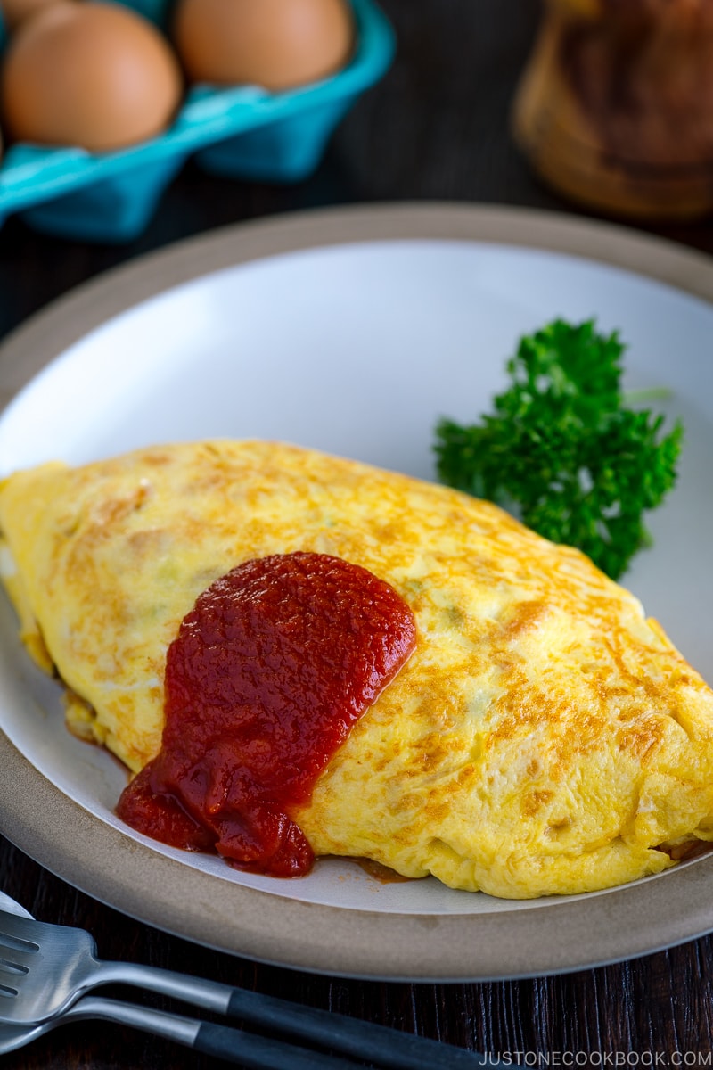 A plate containing Omurice, topped with tomato sauce and garnished with parsley.