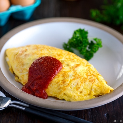 A plate containing Omurice, topped with tomato sauce and garnished with parsley.