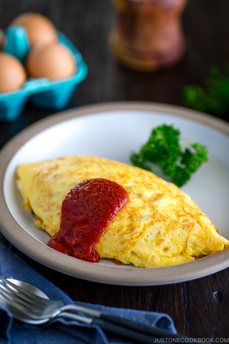 A plate containing Omurice, topped with tomato sauce and garnished with parsley.