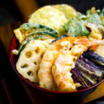 Assorted tempura served on a bed of steamed rice in a red lacquered bowl.