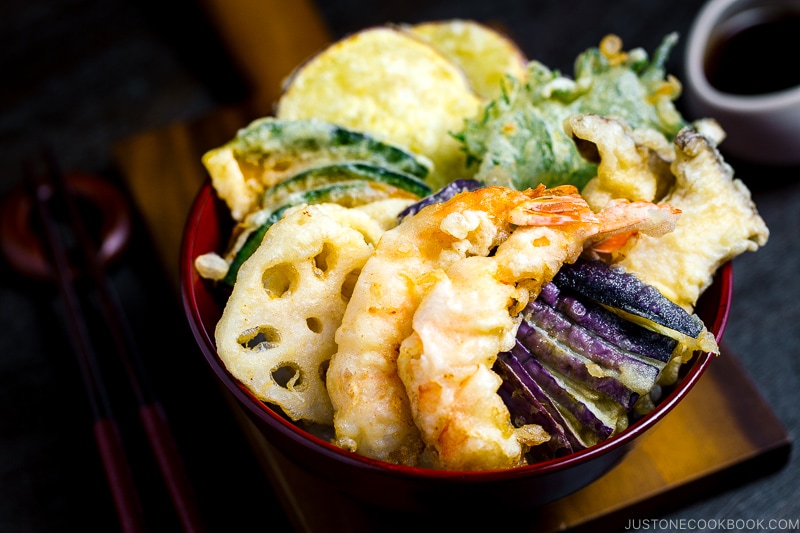 Assorted tempura served on a bed of steamed rice in a red lacquered bowl.