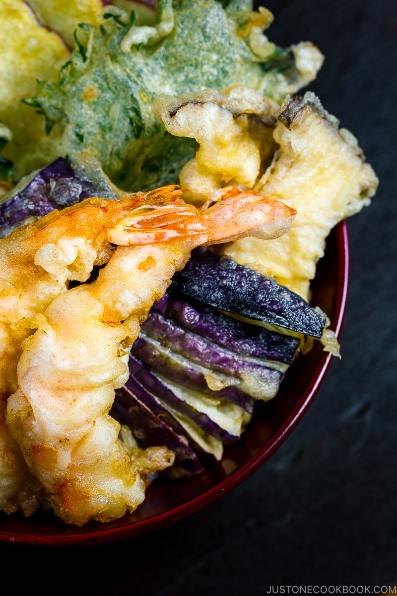 Assorted tempura served on a bed of steamed rice in a red lacquered bowl.