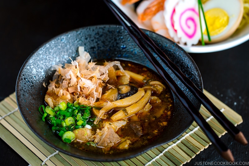 A black bowl of Tsukemen dipping sauce and a white bowl containing noodles with toppings.