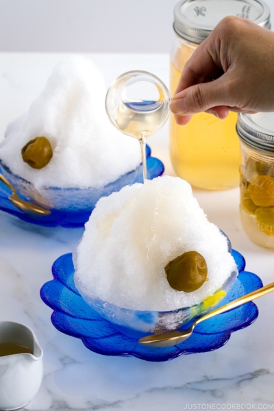 Ume syrup pouring over Ume Shaved Ice served on a blue glass plate.