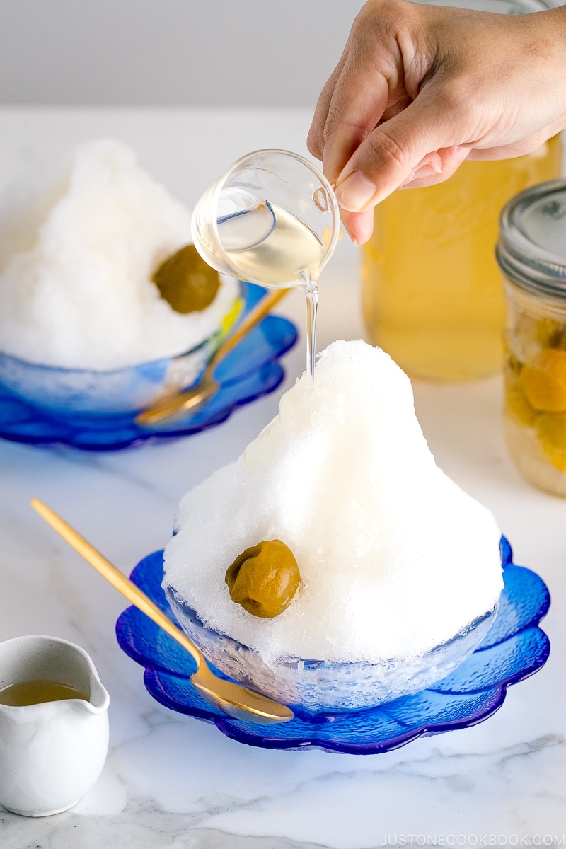 Ume syrup pouring over Ume Shaved Ice served on a blue glass plate.