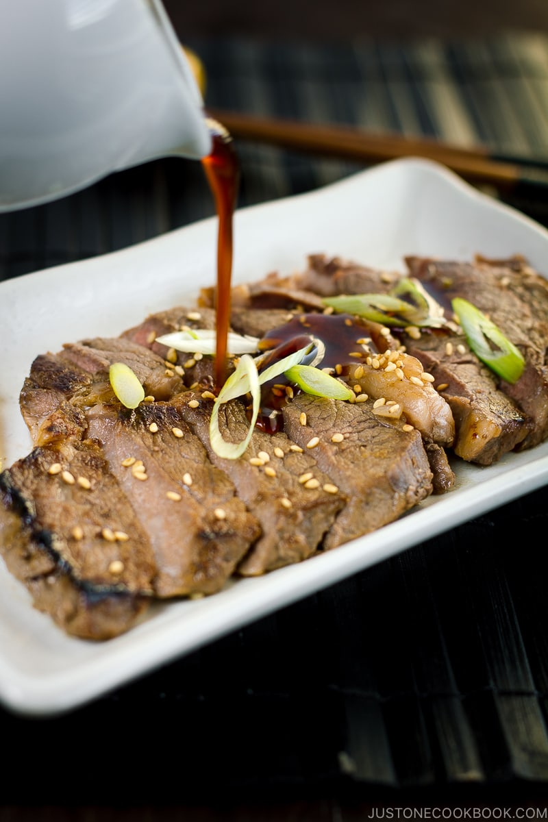 Teriyaki sauce is drizzling over beef teriyaki on a white plate.