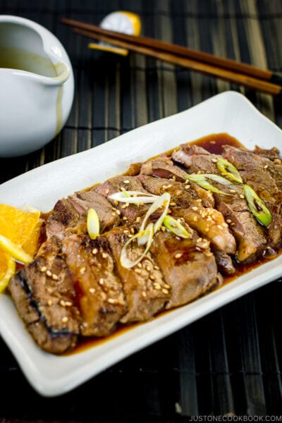 A white plate containing beef teriyaki sprinkled with sesame seeds and scallion.