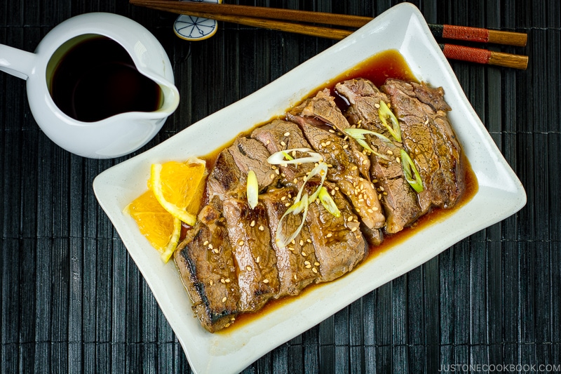 A white plate containing beef teriyaki sprinkled with sesame seeds and scallion.