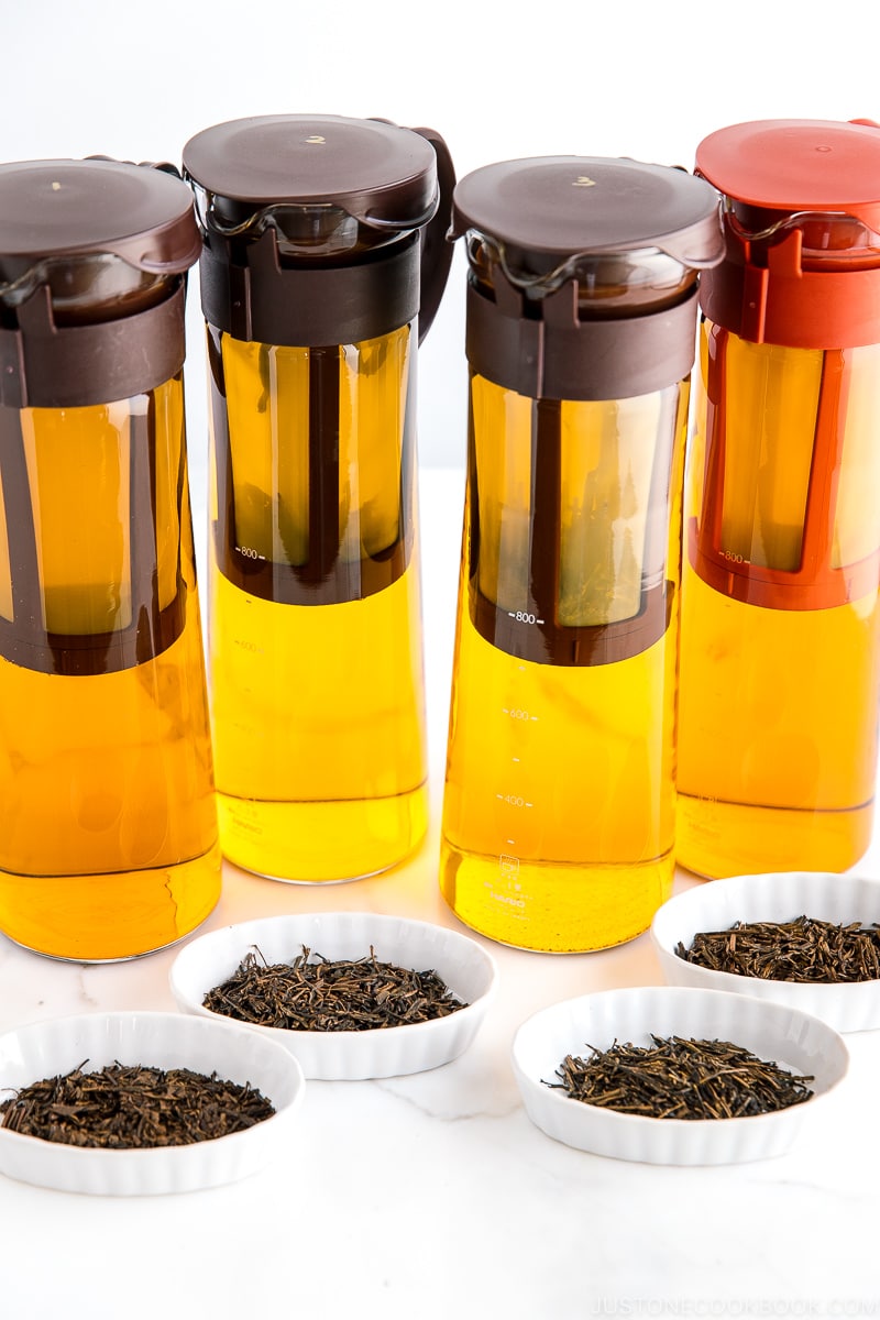 different types of hojicha tea leaves in white dish in front of cold brew hojicha