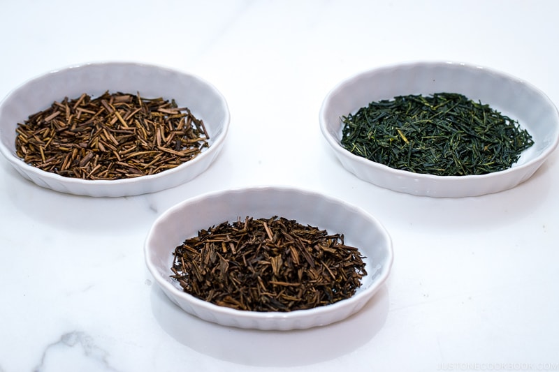 different types of tea leaves in white dishes on marble table