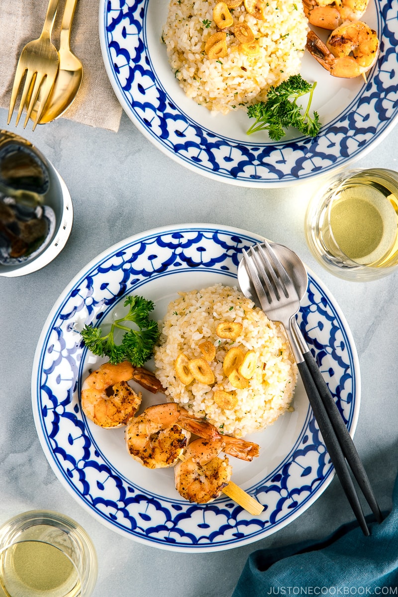 A blue and white plate containing garlic fried rice and skewered grilled shrimp.