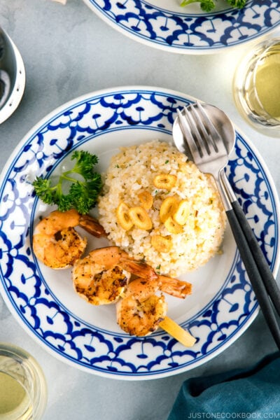 A blue and white plate containing garlic fried rice and skewered grilled shrimp.