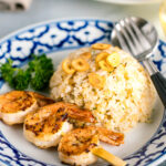 A blue and white plate containing garlic fried rice and skewered grilled shrimp.