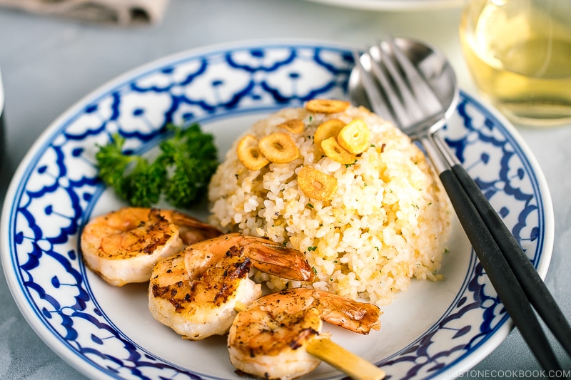 A blue and white plate containing garlic fried rice and skewered grilled shrimp.