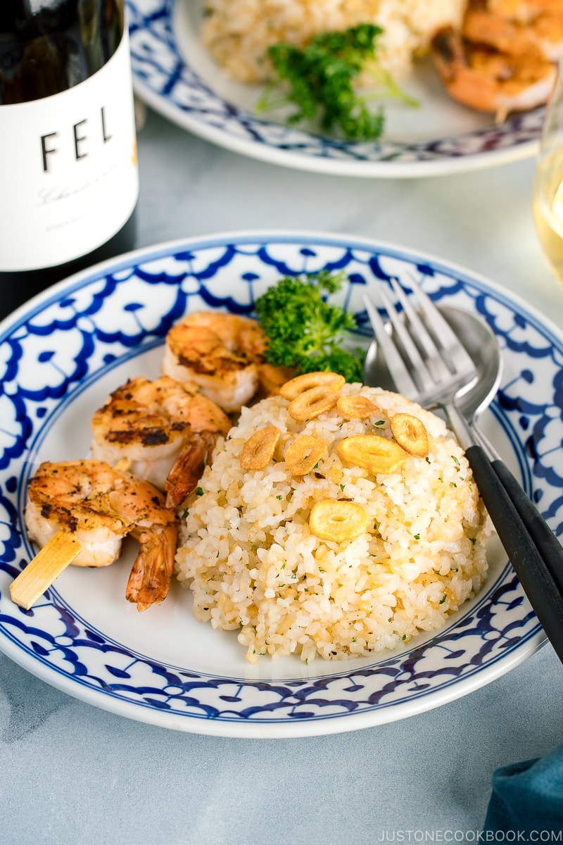 A blue and white plate containing garlic fried rice and skewered grilled shrimp.