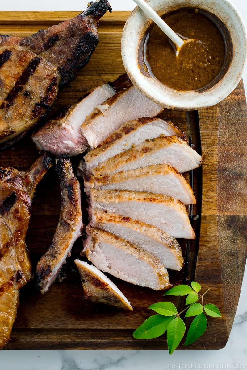 Slices of kurobuta pork chops served on the wooden cutting board with the bowl oof yuzu kosho flavored miso sauce.