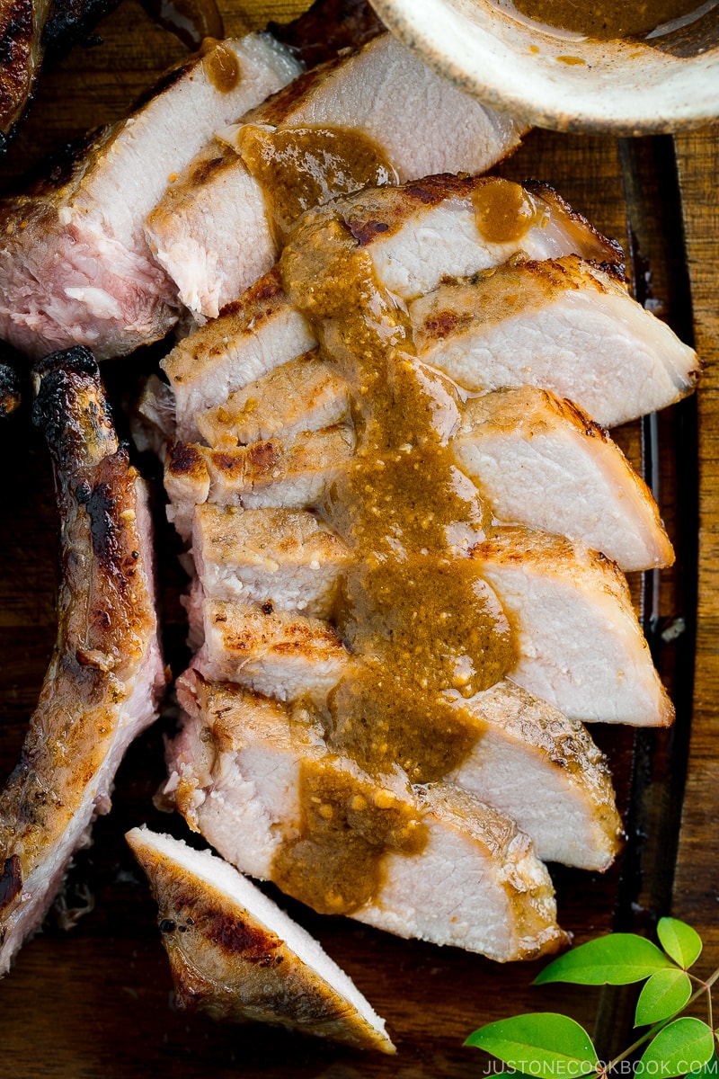 Slices of kurobuta pork chops served on the wooden cutting board with the drizzle of yuzu kosho flavored miso sauce.