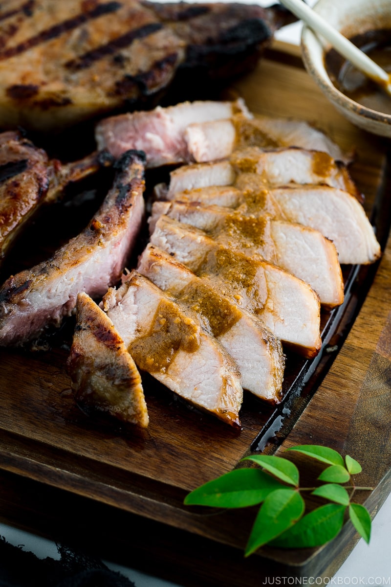 Slices of kurobuta pork chops served on the wooden cutting board with the drizzle of yuzu kosho flavored miso sauce.