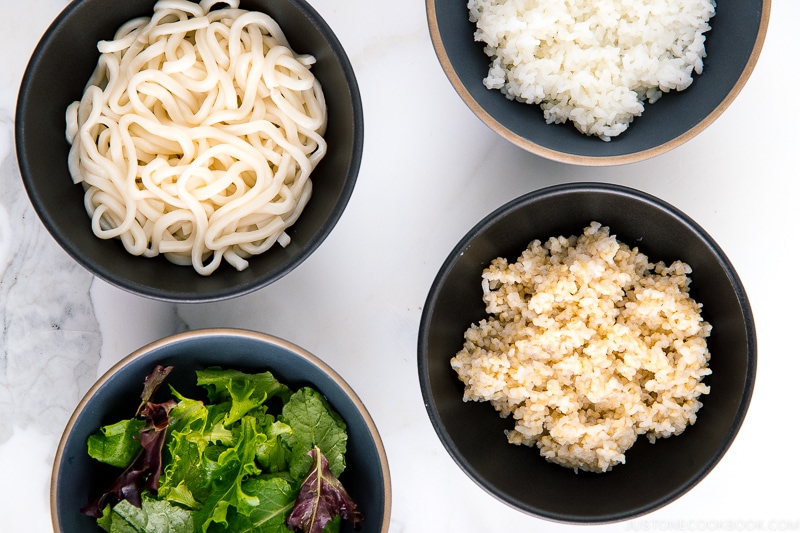 Bowls of carbs; white rice, brown rice, udon noodles, and no carb (leafy greens)