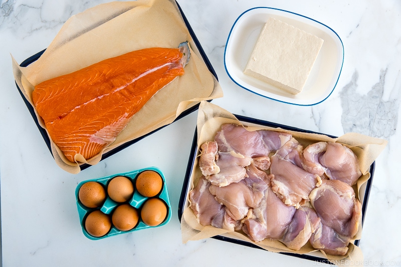 Trays of proteins; salmon, tofu, eggs, and chicken.