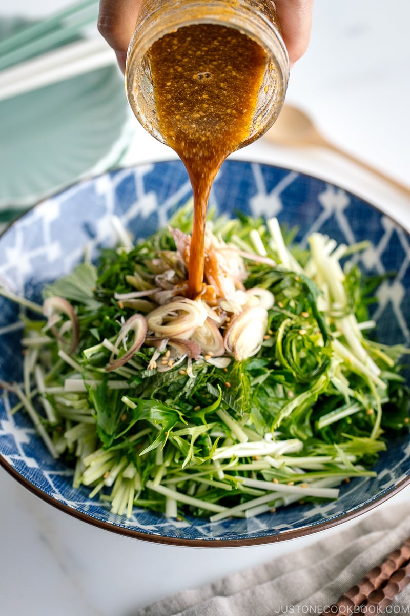 A dressing is pour over Mizuna Myoga Salad in a blue Japanese bowl.