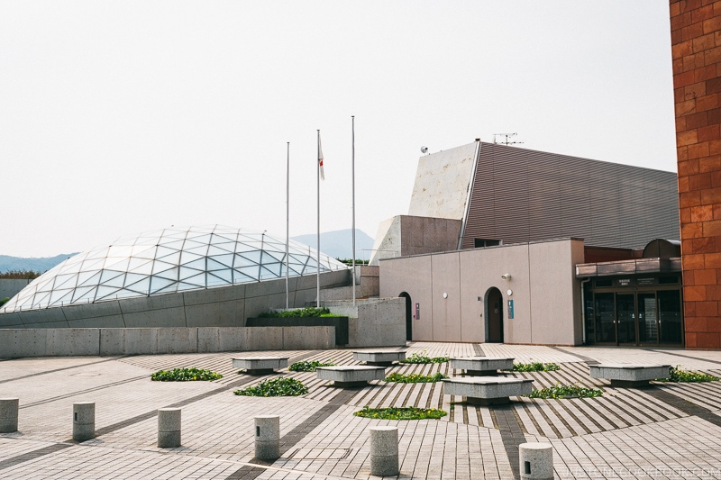 a concrete plaza with glass dome of Nagasaki Atomic Bomb Museum in the back