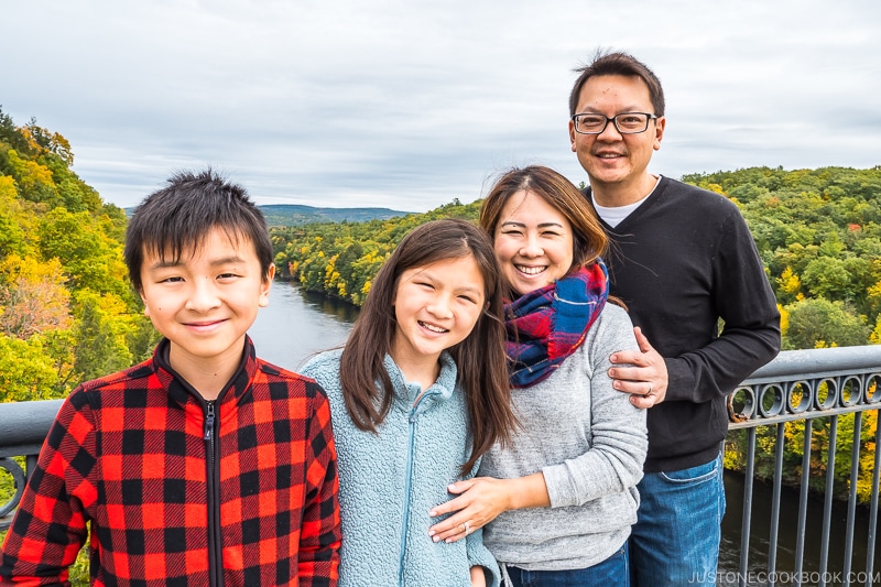 family standing on a bridge above a river with trees in the background