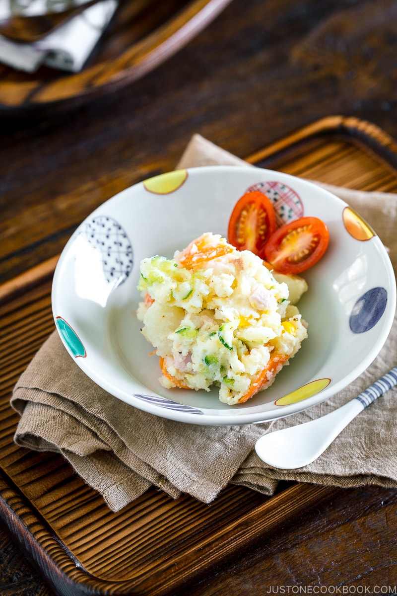 A ceramic bowl containing Japanese potato salad and cherry tomatoes.