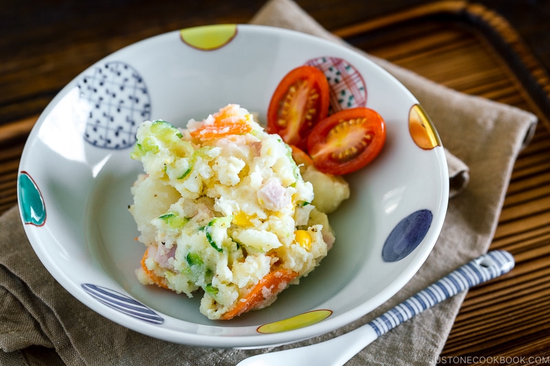 A ceramic bowl containing Japanese potato salad and cherry tomatoes.