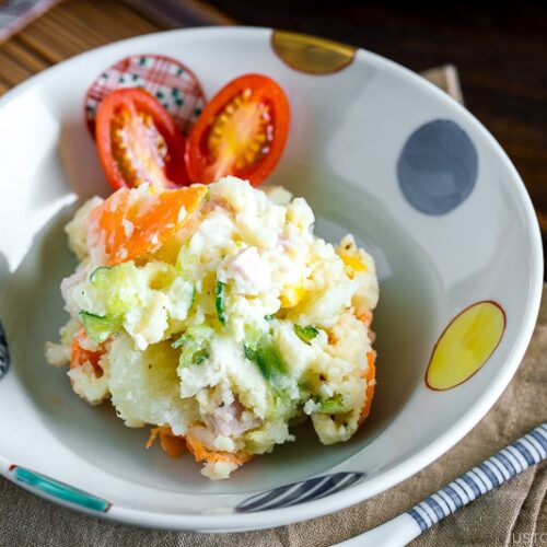 A ceramic bowl containing Japanese potato salad and cherry tomatoes.