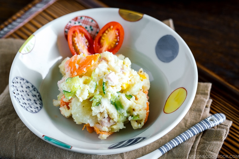 A ceramic bowl containing Japanese potato salad and cherry tomatoes.