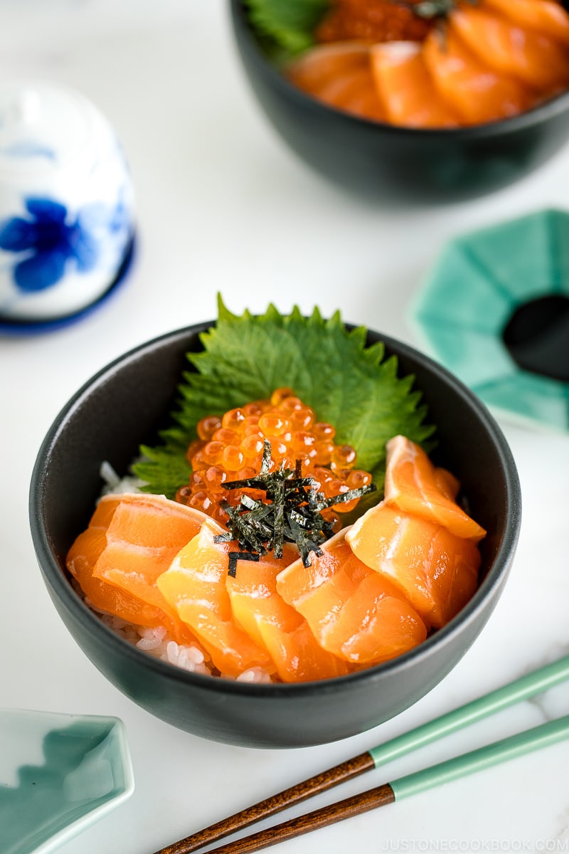A black bowl containing a bed of rice topped with sashimi grade salmon, ikura, and shredded nori.