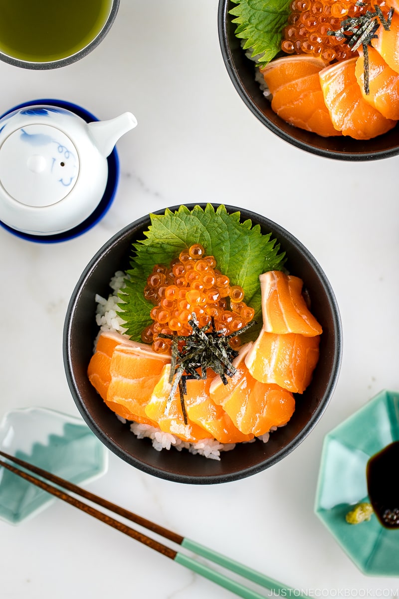 A black bowl containing a bed of rice topped with sashimi grade salmon, ikura, and shredded nori.