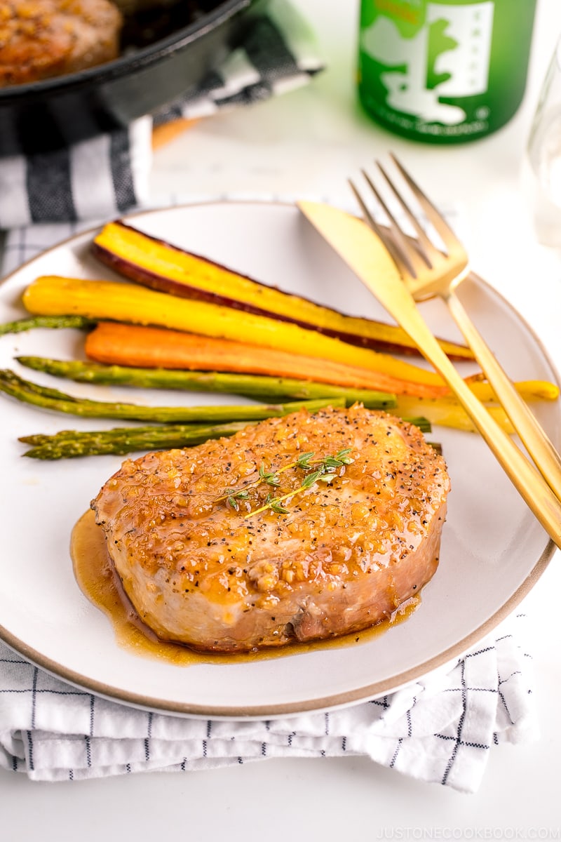 A white plate containing honey garlic pork chops, roasted carrot, and asparagus.