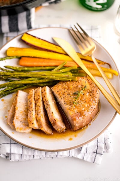 A white plate containing honey garlic pork chops, roasted carrot, and asparagus.