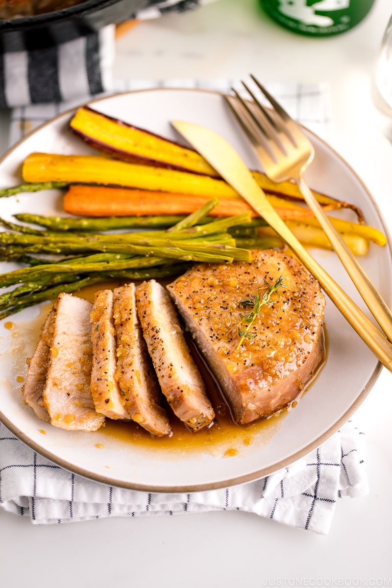 A white plate containing honey garlic pork chops, roasted carrot, and asparagus.