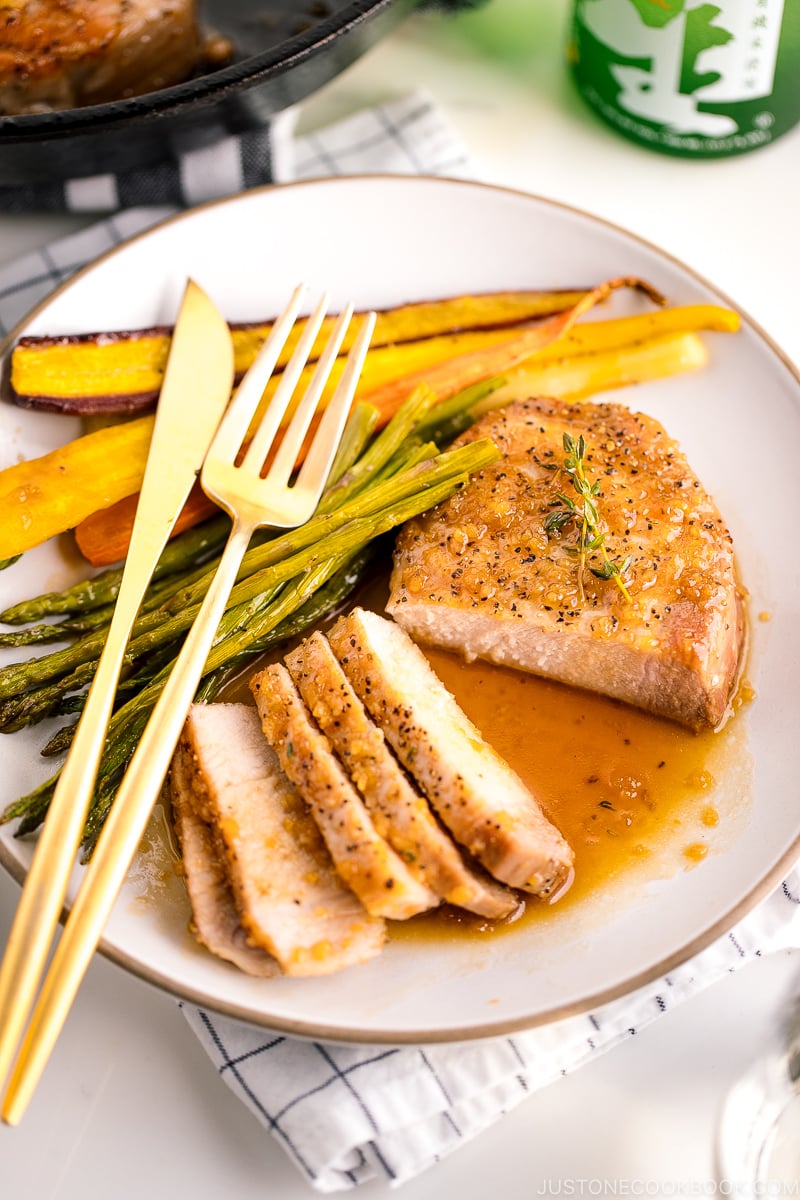 A white plate containing honey garlic pork chops, roasted carrot, and asparagus.