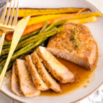 A white plate containing honey garlic pork chops, roasted carrot, and asparagus.