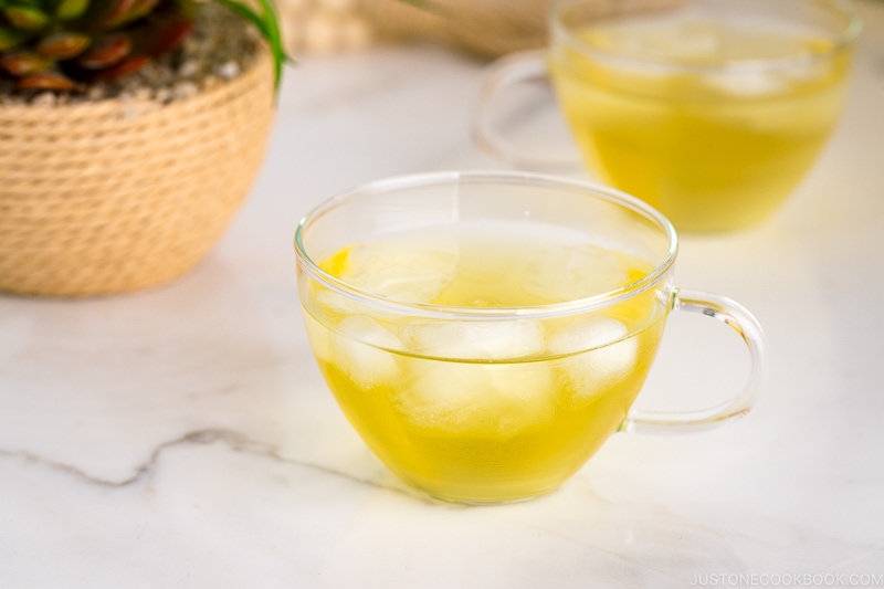 green iced tea in a glass cup on top of marble table next to a plant